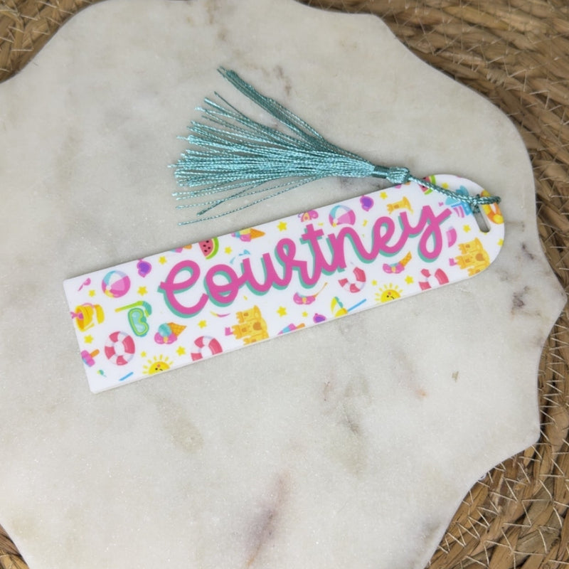 A personalized fabric bookmark with the name 'Courtney' in pink script, decorated with colorful beach scene and finished with a light blue tassel. 