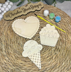 Wooden cutouts of a heart, cupcake, and ice cream cone with paint containers.