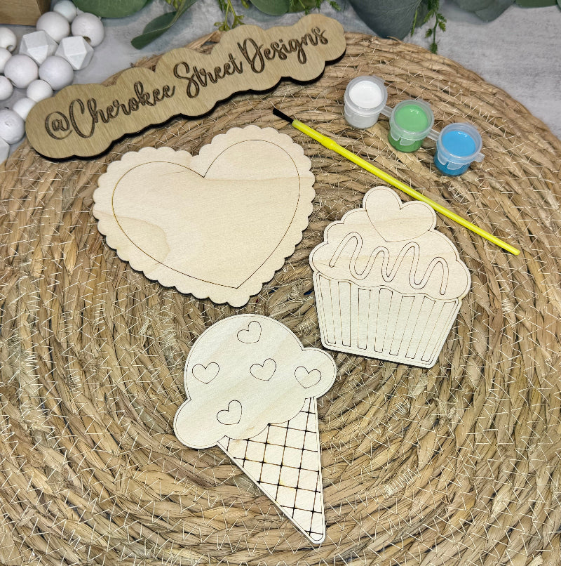 Wooden cutouts of a heart, cupcake, and ice cream cone with paint containers.