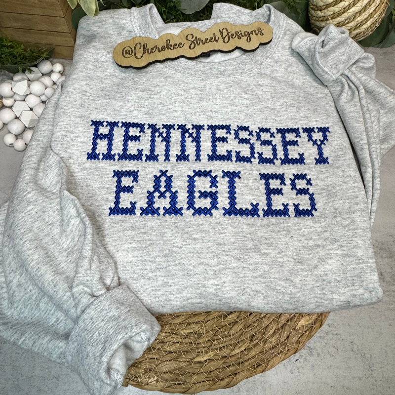 Gray sweatshirt with 'HENNESSEY EAGLES' text on a wooden surface with decorative items.