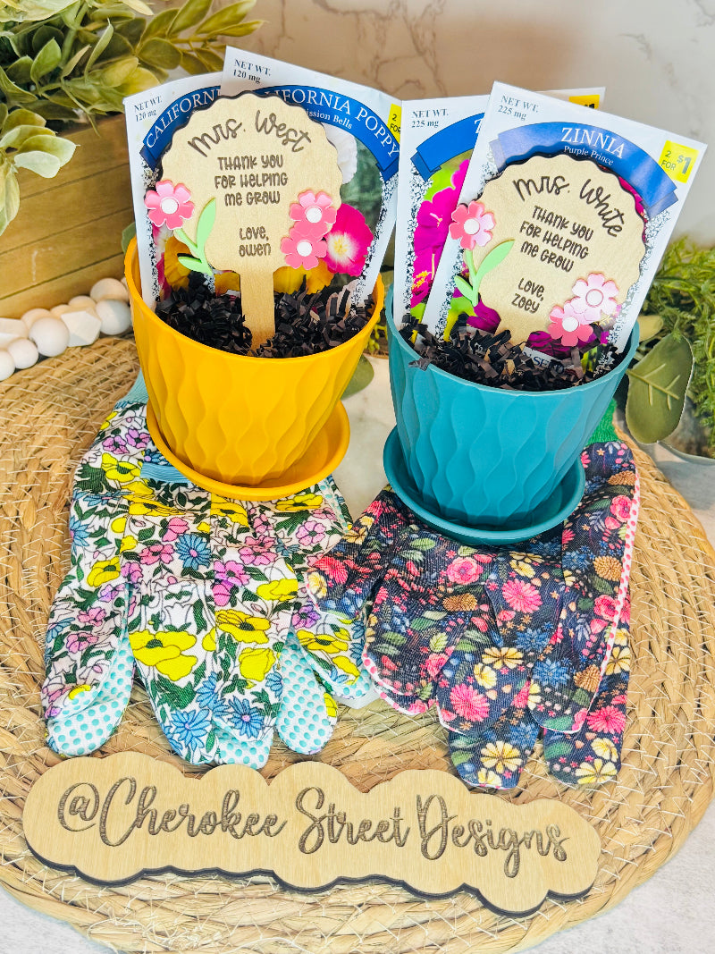 Two potted plants with seed packets and gardening gloves on a woven mat, featuring 'Cherokee Street Designs' branding.