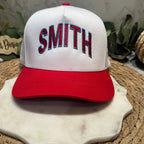 White cap with red brim and 'SMITH' in blue and red on a marble surface.
