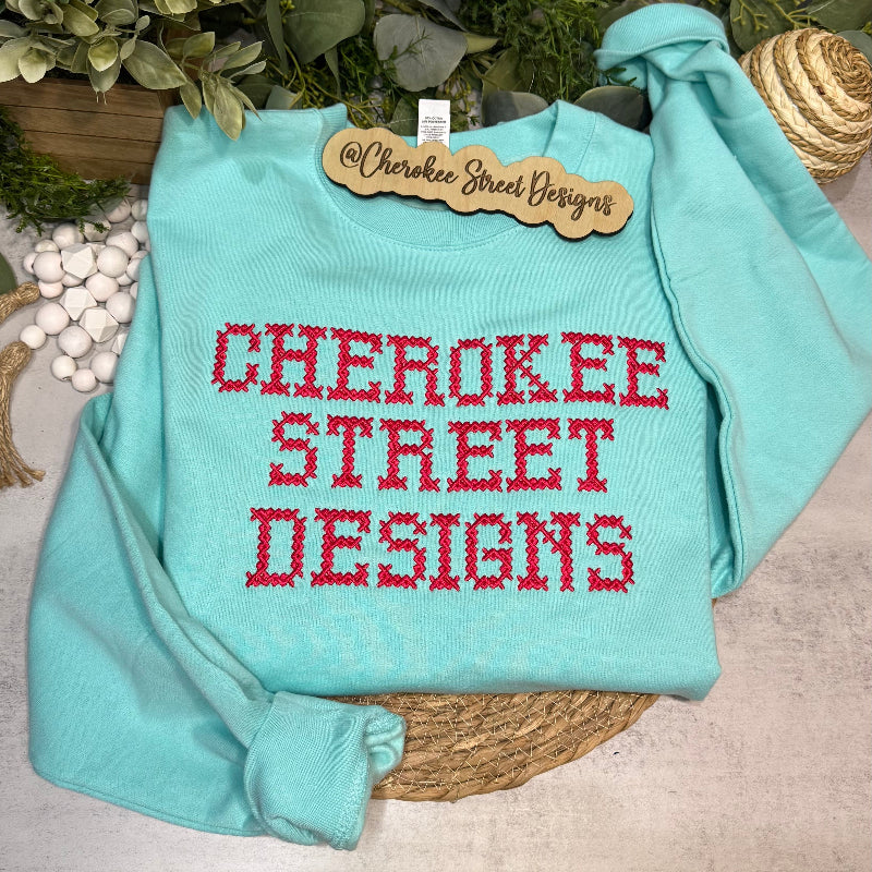 Light blue sweatshirt with red text 'Cherokee Street Designs' on a neutral background