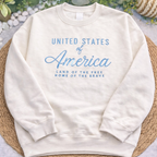White sweatshirt with 'United States of America' text on a woven mat with greenery in the background