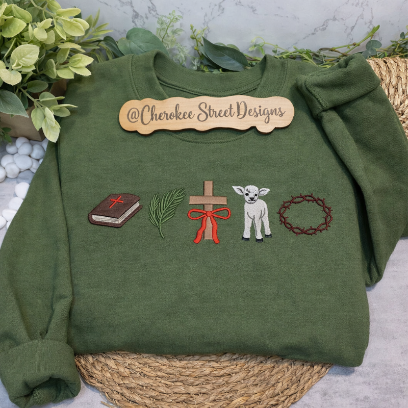 Green sweatshirt with embroidered designs and 'Cherokee Street Designs' label on a textured surface.