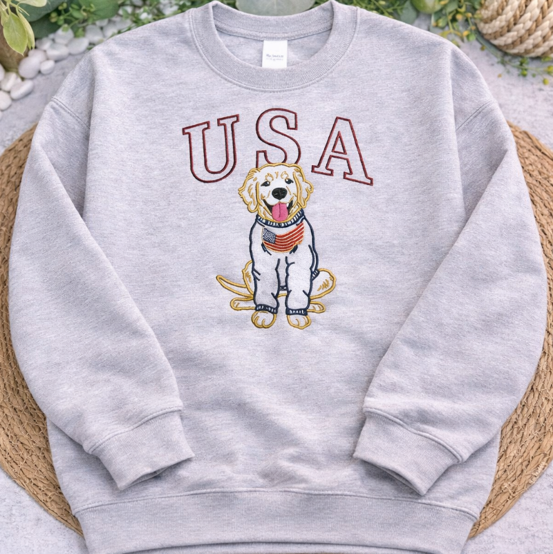 Gray sweatshirt with 'USA' and dog illustration on a textured surface with greenery.