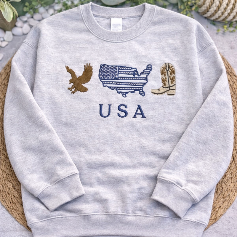 Gray sweatshirt with USA-themed graphics on a textured surface with greenery