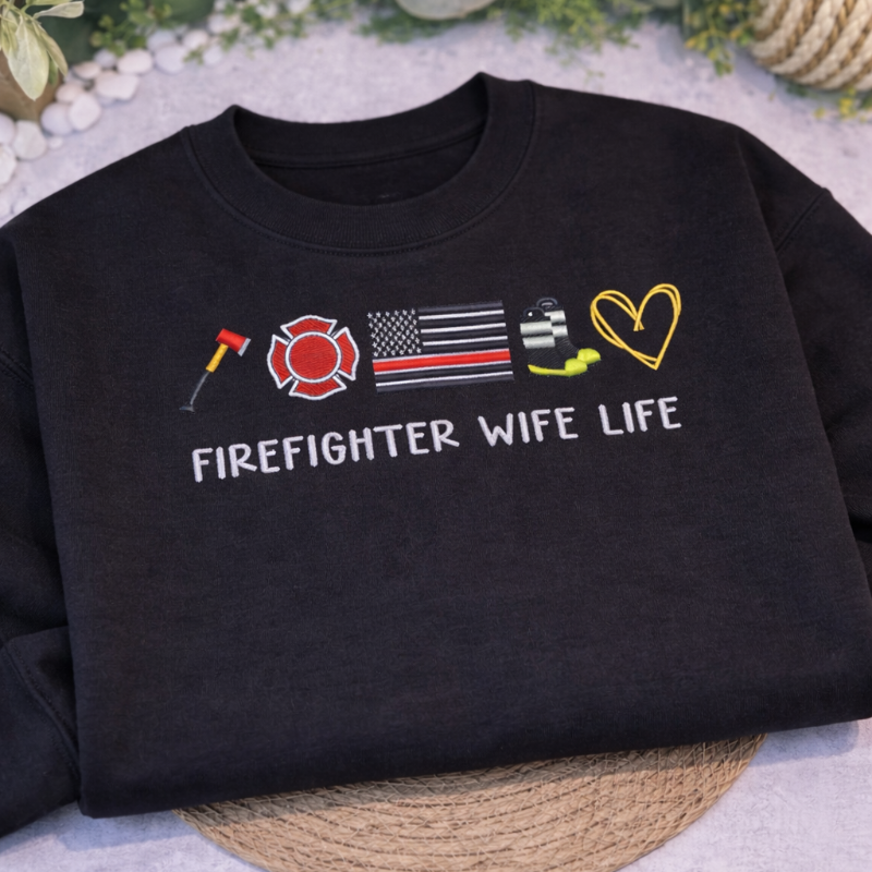 Black sweatshirt with embroidered graphics and 'Firefighter Wife Life' text on a textured surface.
