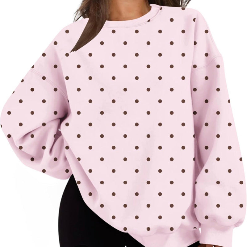 A woman wearing a light pink long-sleeve sweatshirt with a dark brown polka dot pattern, paired with black shorts, shown against a plain white background.