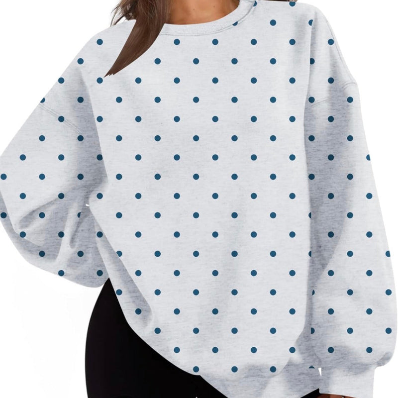 A woman wearing a white long-sleeve crewneck sweatshirt with a navy blue polka dot pattern, paired with black shorts.