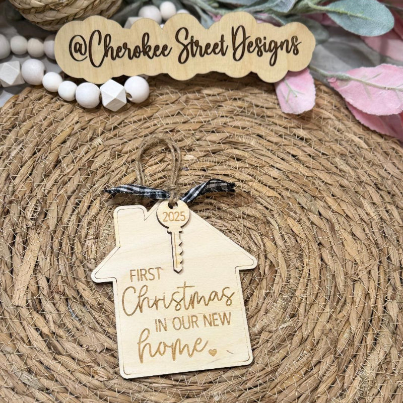 Wooden house-shaped ornament with 'First Christmas in Our New Home' text branding.