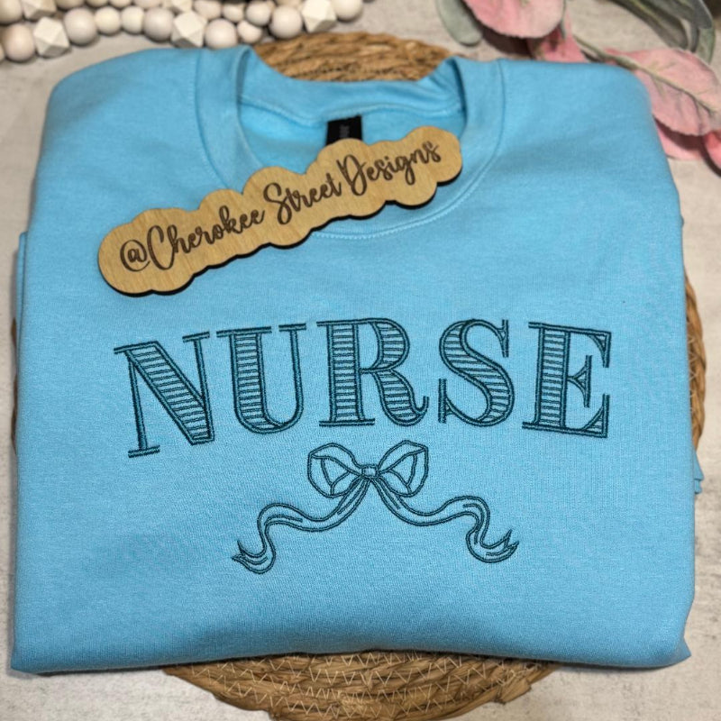 Blue sweatshirt with 'NURSE' text and a bow design