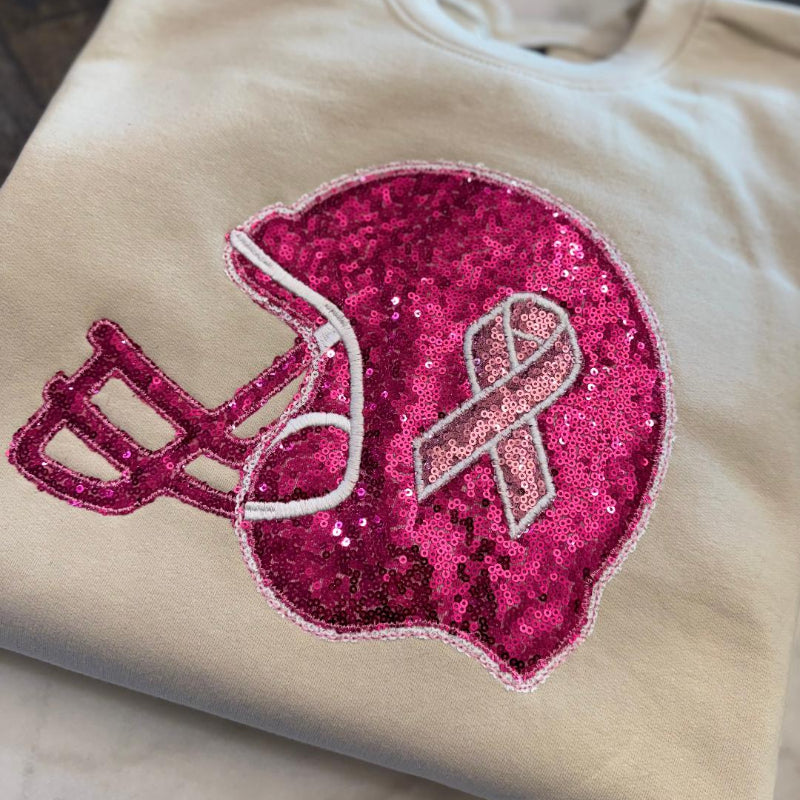 Beige sweatshirt with pink sequin football helmet and breast cancer awareness ribbon design.